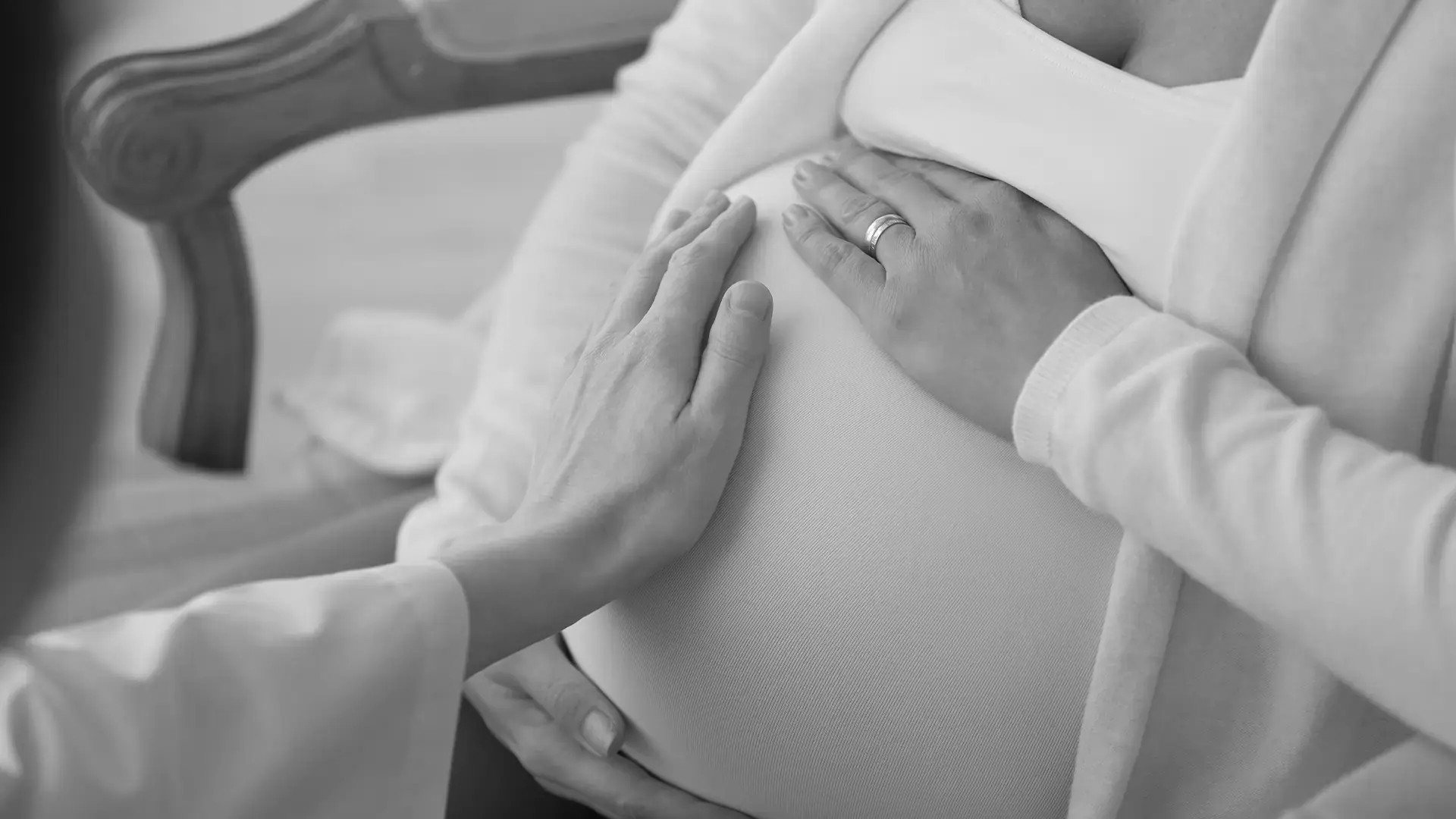 A doula and midwife's hands resting together on a pregnant belly during a prenatal visit